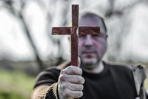 Un monje sostiene una cruz cristiana de madera frente a él.